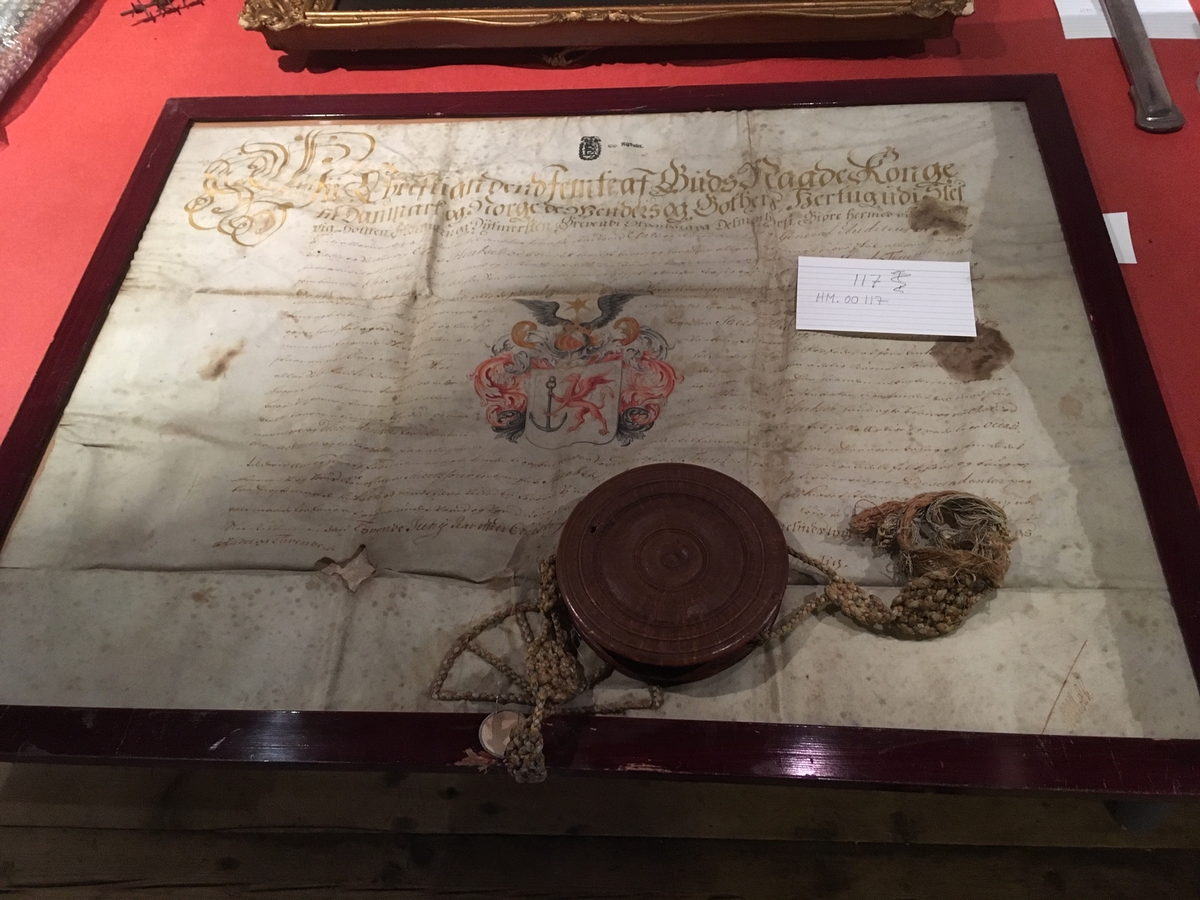 Diplom i ramme, med vokssegl i dreiet treboks, med gjenget lokk. Adelsdiplom fra år 1660 for familien Hübsch.