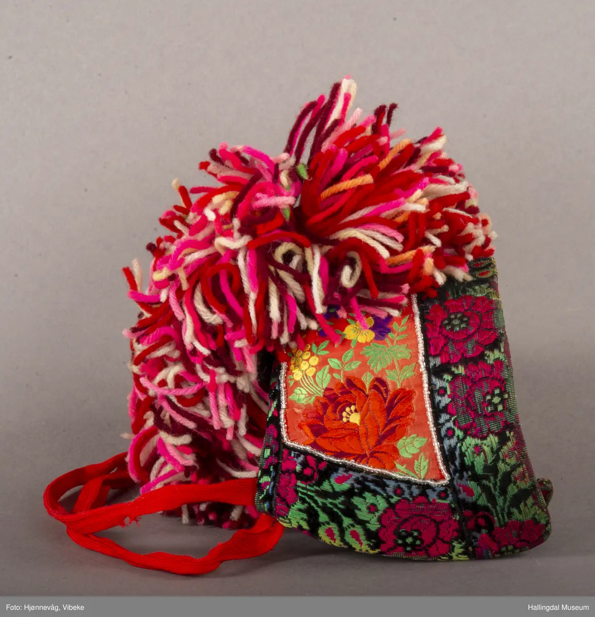 a) Jentepannelin av papp, sylkjety, bolu, kårilsteinar, bomullsty, ullgarn, sydd.
b) Nakkeskuve av flanillsgarn i raudt, mørk raudt, lys raudt, kvitt, lys gult, og grønt.