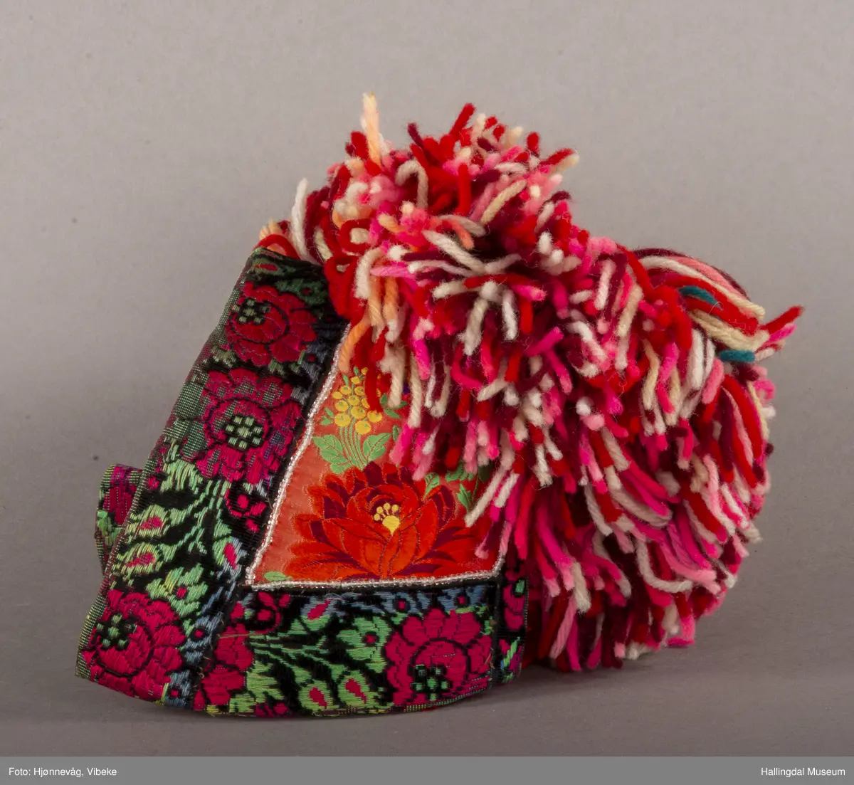 a) Jentepannelin av papp, sylkjety, bolu, kårilsteinar, bomullsty, ullgarn, sydd.
b) Nakkeskuve av flanillsgarn i raudt, mørk raudt, lys raudt, kvitt, lys gult, og grønt.