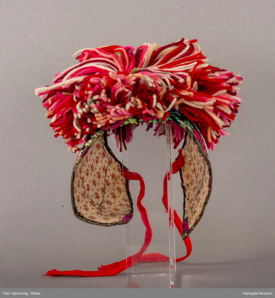 a) Jentepannelin av papp, sylkjety, bolu, kårilsteinar, bomullsty, ullgarn, sydd.
b) Nakkeskuve av flanillsgarn i raudt, mørk raudt, lys raudt, kvitt, lys gult, og grønt.