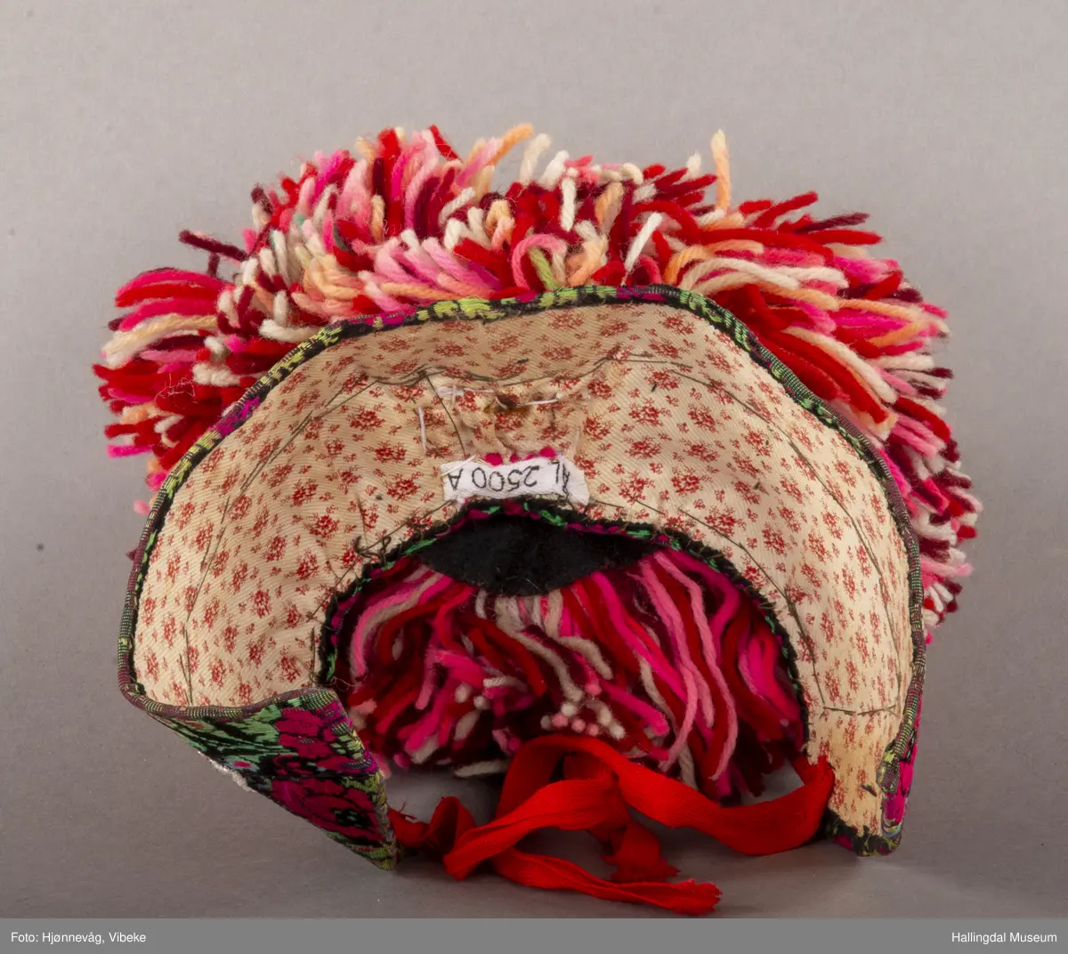 a) Jentepannelin av papp, sylkjety, bolu, kårilsteinar, bomullsty, ullgarn, sydd.
b) Nakkeskuve av flanillsgarn i raudt, mørk raudt, lys raudt, kvitt, lys gult, og grønt.