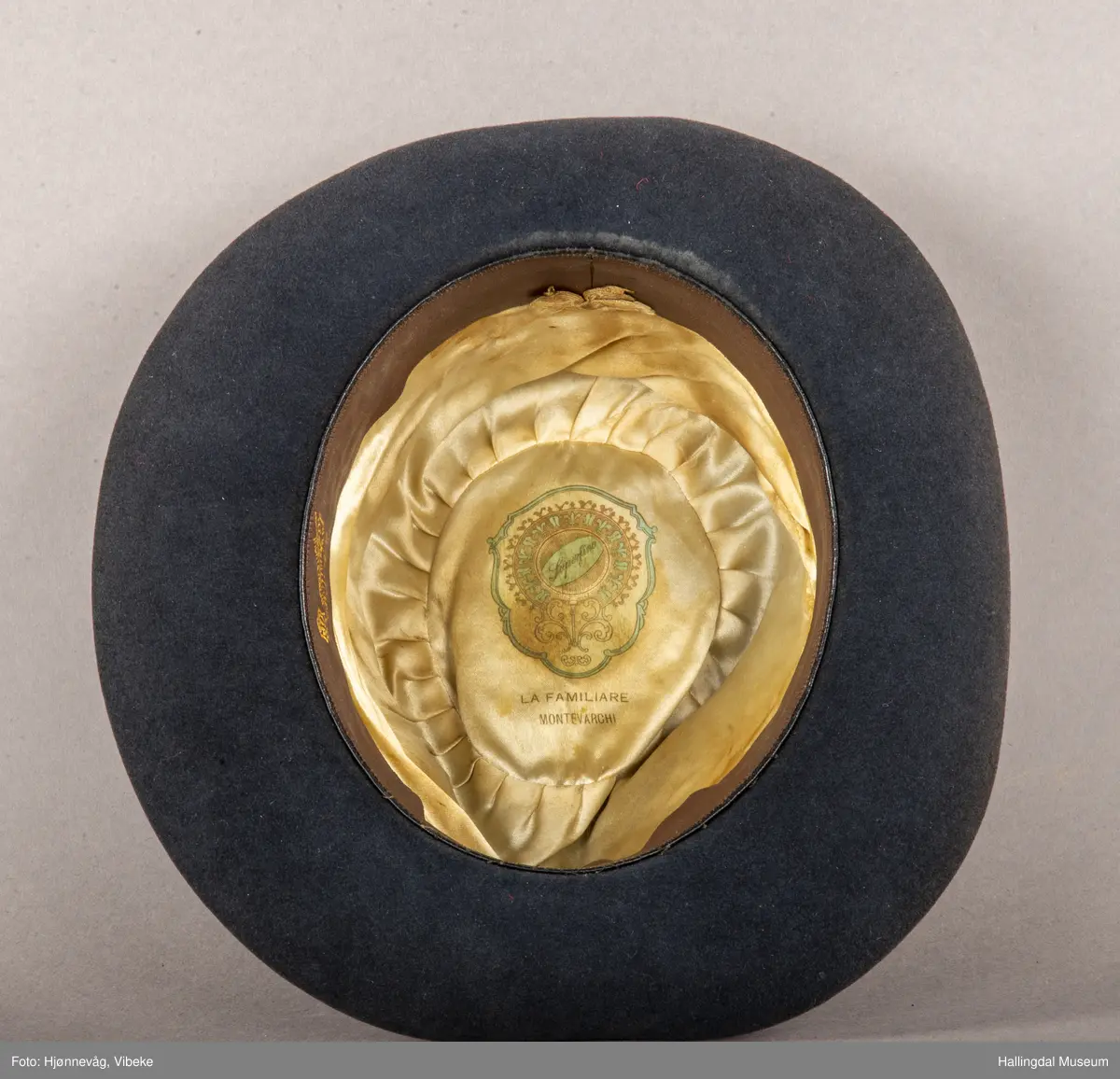 Filthatt med et bredt silkebånd rundt pullen. Høyde: 12 cm, Bredde brem: 6,5 cm. Gråbrun.
