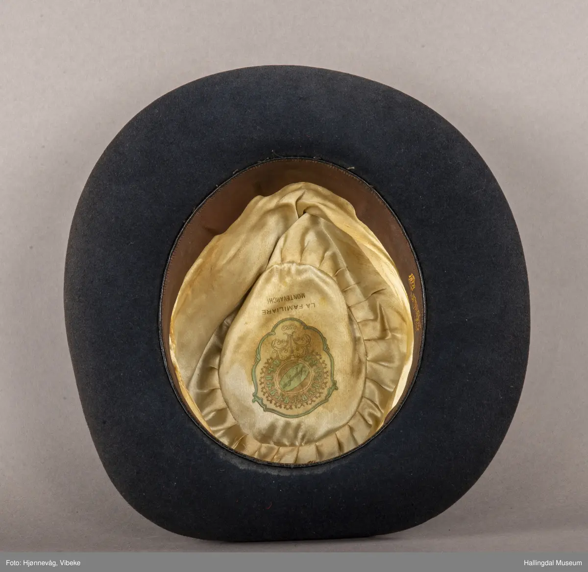 Filthatt med et bredt silkebånd rundt pullen. Høyde: 12 cm, Bredde brem: 6,5 cm. Gråbrun.