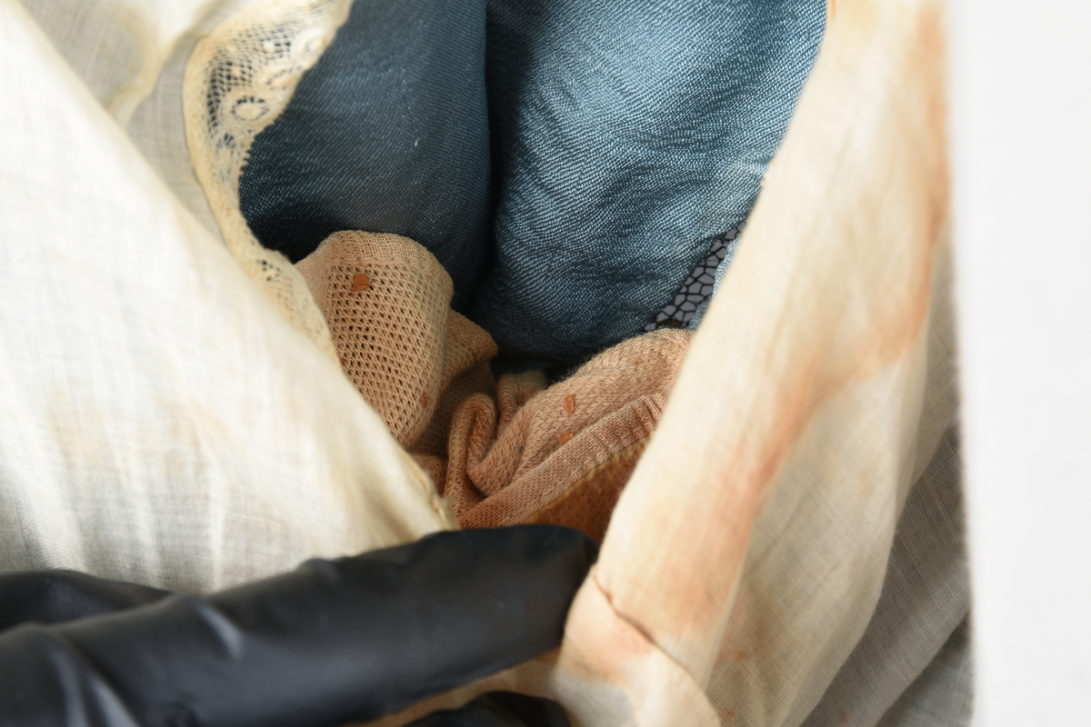 Fotsid kjole i lyseblå silke-duchesse. Blylodd nederst i kanten. Den har slep som er festet i livet, drapert og med blylodd nede. Kjolen er avdelt i livet og har drapert belte i kjolestoffet som lukkes med hekter. Den har 32 cm lange isydde ermer. Utover ermene er det trukket mørkere blå tyll brodert med gullfarget metalltråd. Stoffet på skuldrene er trukket noe utover ermene. Kjolen har V-utringning foran og bak, kantet med samme stoffet som er trukket utenpå ermene. V-utringningene er dekket med tynn hvit bomull belagt med kniplingsbroderi. Livet er fóret med hvit lerret. Kjolen lukkes bak med hekter og trykknapper.