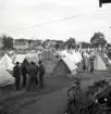 Oxtorget, midsommardagen 1942. Vy över en massa olika tält. I förgrunden syns en mängd cyklar och i bakgrunden syns ett antal bostadshus.