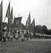 Lantbruksutställning 1942.
En fanborg med människor i olika folkdräkter (bl a Värendsdräkter) tågar in på skolgården till Växjö Högre Allmänna Läroverk.