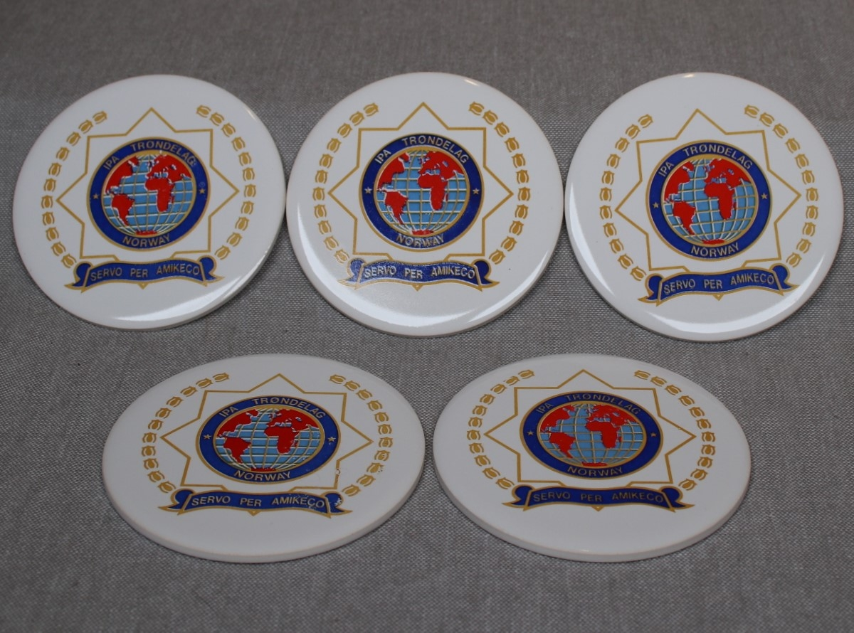 Runde, hvite porselensplaketter påtrykt IPAs emblem og motto.