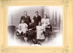 Familjeporträtt på bröllopsdagen den 17 maj 1895. En man, hans hustru och fem barn avbildade tillsamman med en hund och en katt.
Famijlen är inte namngiven på fotot. 
Handskriven text på tillhörande pappskiva 