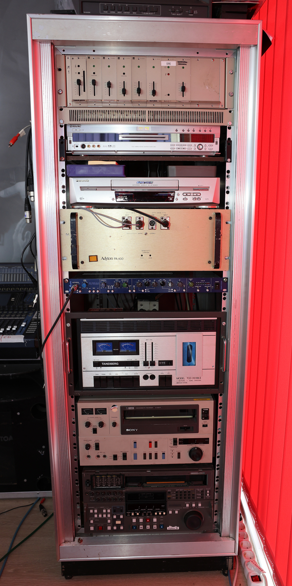 Studio med miksebord og monitorer og separat rack med lydmikser.