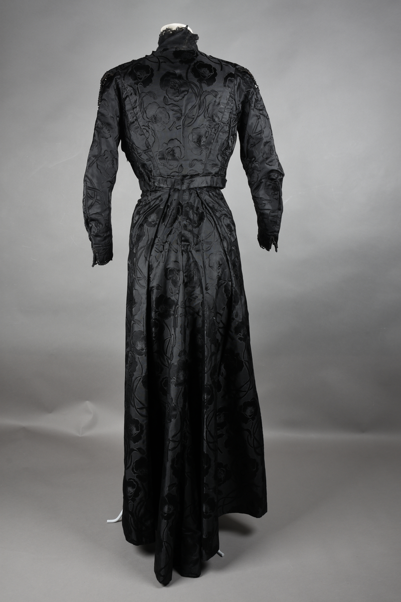 Kjoleliv av sort brokade. Silkeinnfelling og tyllinnfelling foran. Stjernekrave besatt med slag av paljetter og perler. Høy halslinning. Brokaden har et valmuemønster (jugend).