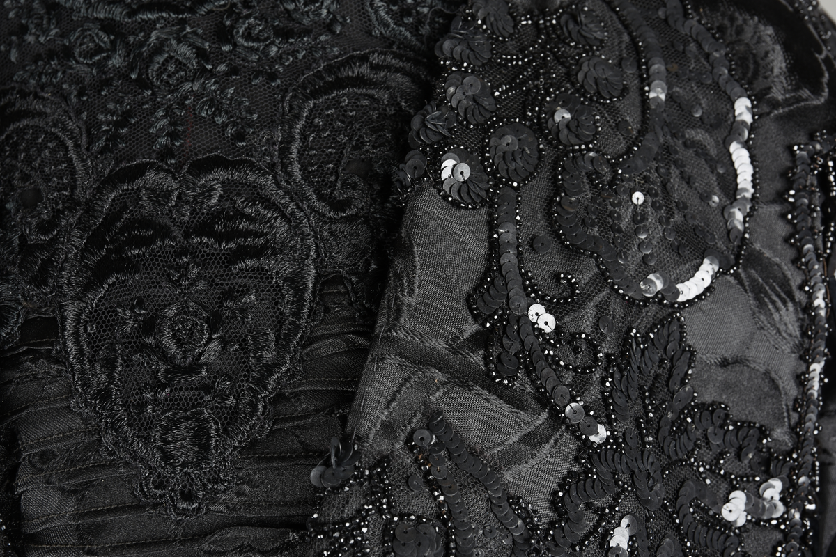 Kjoleliv av sort brokade. Silkeinnfelling og tyllinnfelling foran. Stjernekrave besatt med slag av paljetter og perler. Høy halslinning. Brokaden har et valmuemønster (jugend).