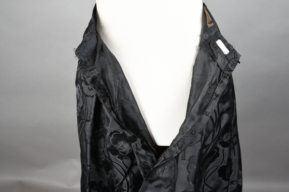 Skjørt av brokade med valmuemønster (jugend). Slep bak og ekstra vidde over setet hvor det er plass til en kø.