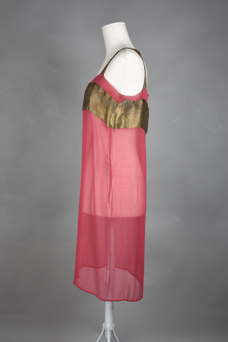 Løs underkjole av bringebærrød chiffon. Rett fasong. Et bredt bronsebånd rundt brystet. To doble skulderstropper (krysset over skulderen) av bronsebånd. Blybånd i nedre kant for å holde kanten nede.