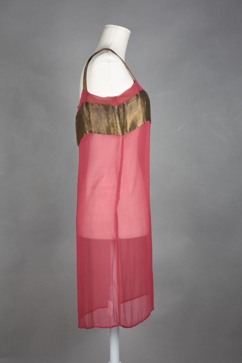 Løs underkjole av bringebærrød chiffon. Rett fasong. Et bredt bronsebånd rundt brystet. To doble skulderstropper (krysset over skulderen) av bronsebånd. Blybånd i nedre kant for å holde kanten nede.