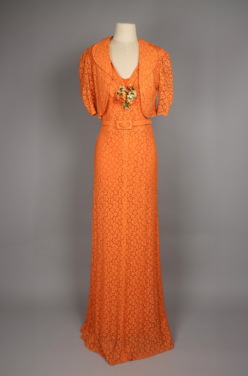 Klänning för dam, vår 1936. Aftonklänning med jacka, orange-färgad bomullsspets. Tillhörande skärp. Stomme av crepe de chine. Hellång. Storlek 38