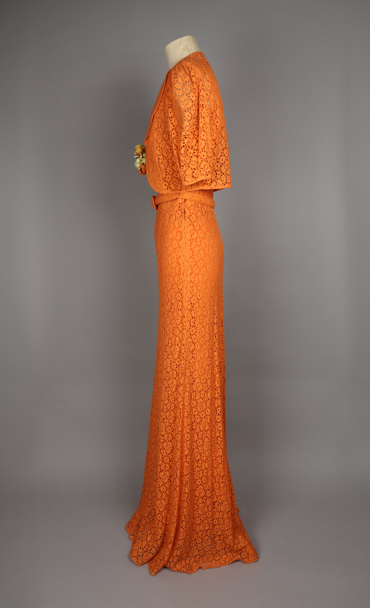 Klänning för dam, vår 1936. Aftonklänning med jacka, orange-färgad bomullsspets. Tillhörande skärp. Stomme av crepe de chine. Hellång. Storlek 38