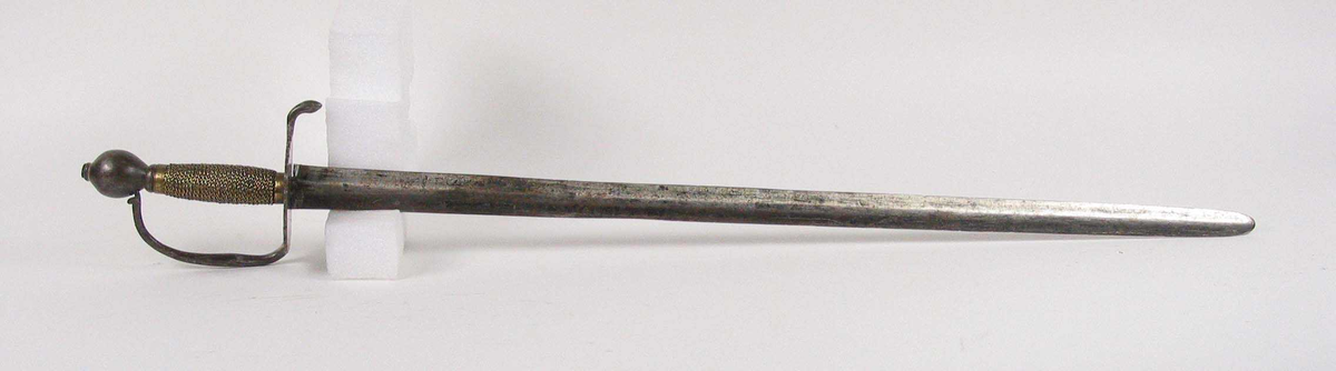 Soldatkorde av type M1701. Pæreformet knapp med nitteknapp. Fliket nyreformet parerplate med nedbøyd bakre parerstang. Fremre parerstang går over i håndbøylen som er tappet inn i knappen. Grepet har snodd messingtråd som avluttes med messingbånd oppe og nede. Rett tveegget klinge med midtås og rester av Fredrik IVs monogram.