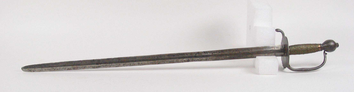 Soldatkorde av type M1701. Pæreformet knapp med nitteknapp. Fliket nyreformet parerplate med nedbøyd bakre parerstang. Fremre parerstang går over i håndbøylen som er tappet inn i knappen. Grepet har snodd messingtråd som avluttes med messingbånd oppe og nede. Rett tveegget klinge med midtås og rester av Fredrik IVs monogram.