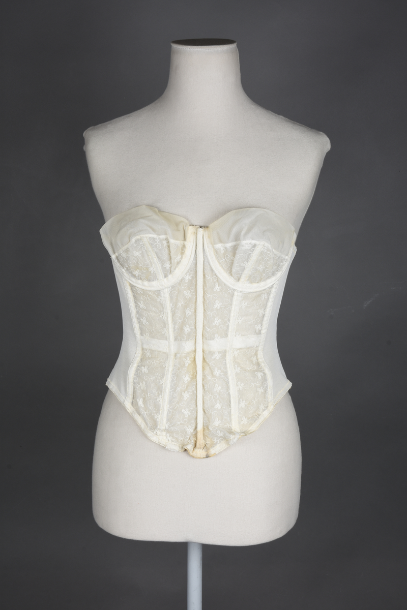 Brystholder av blondestrikk, med spiler. Både korsettspiler og cup-spiler. Lang form. Lukkes bak med hekter.