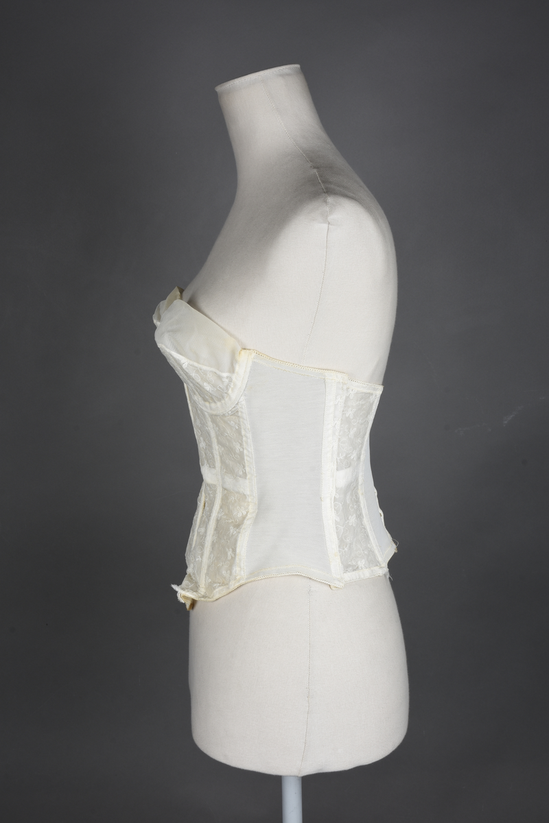 Brystholder av blondestrikk, med spiler. Både korsettspiler og cup-spiler. Lang form. Lukkes bak med hekter.