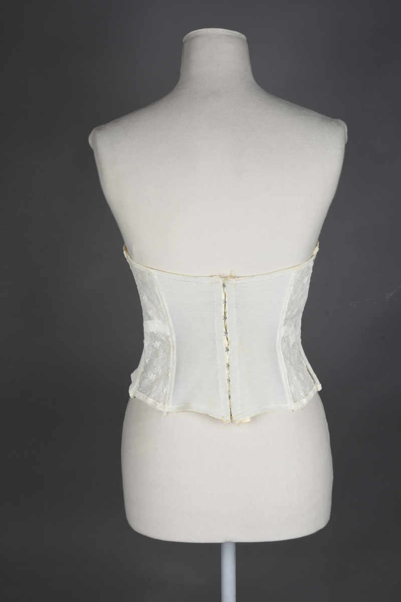 Brystholder av blondestrikk, med spiler. Både korsettspiler og cup-spiler. Lang form. Lukkes bak med hekter.