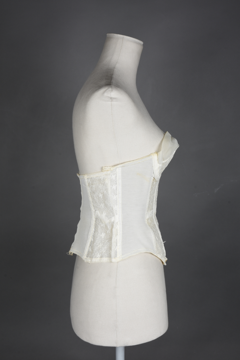 Brystholder av blondestrikk, med spiler. Både korsettspiler og cup-spiler. Lang form. Lukkes bak med hekter.