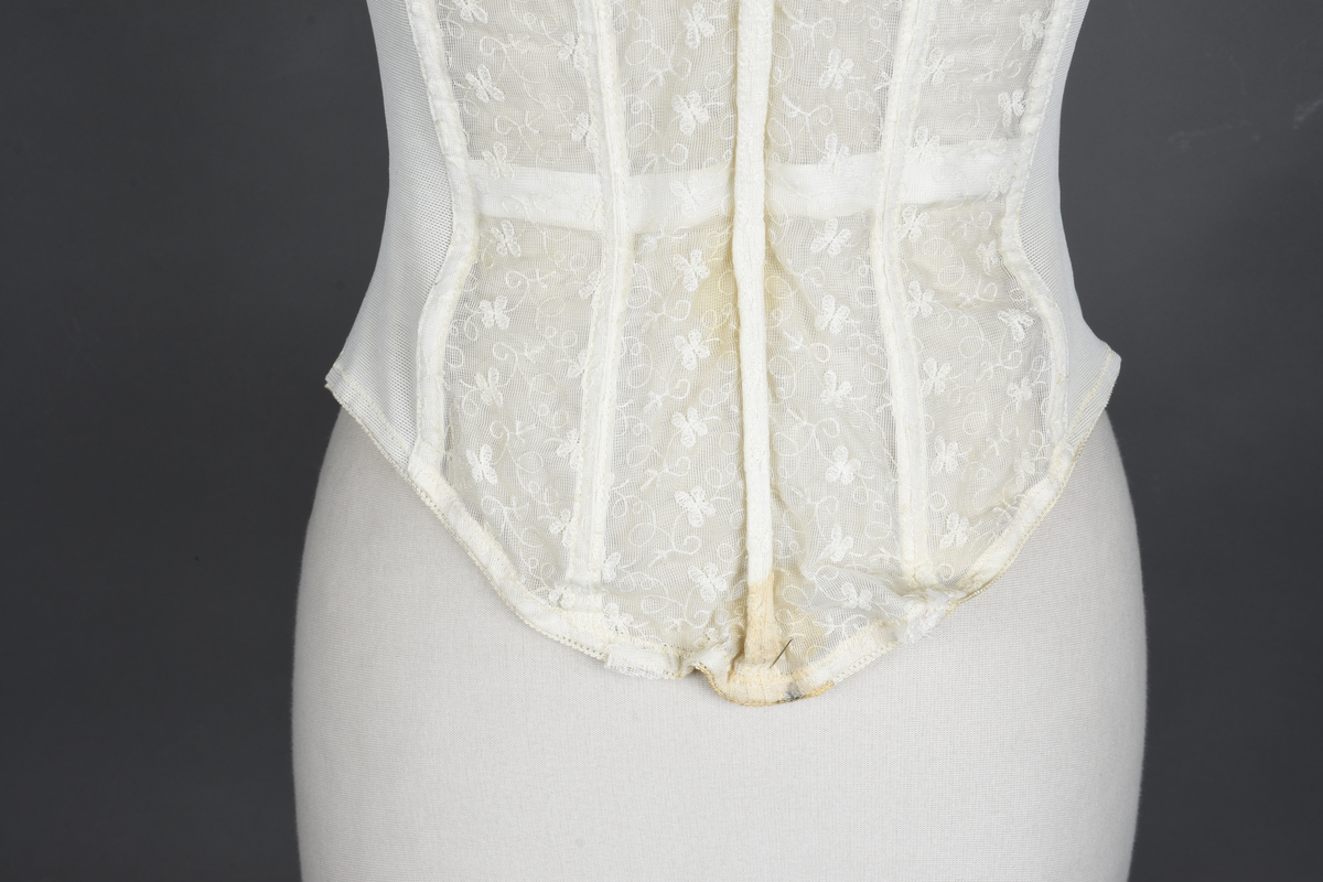 Brystholder av blondestrikk, med spiler. Både korsettspiler og cup-spiler. Lang form. Lukkes bak med hekter.