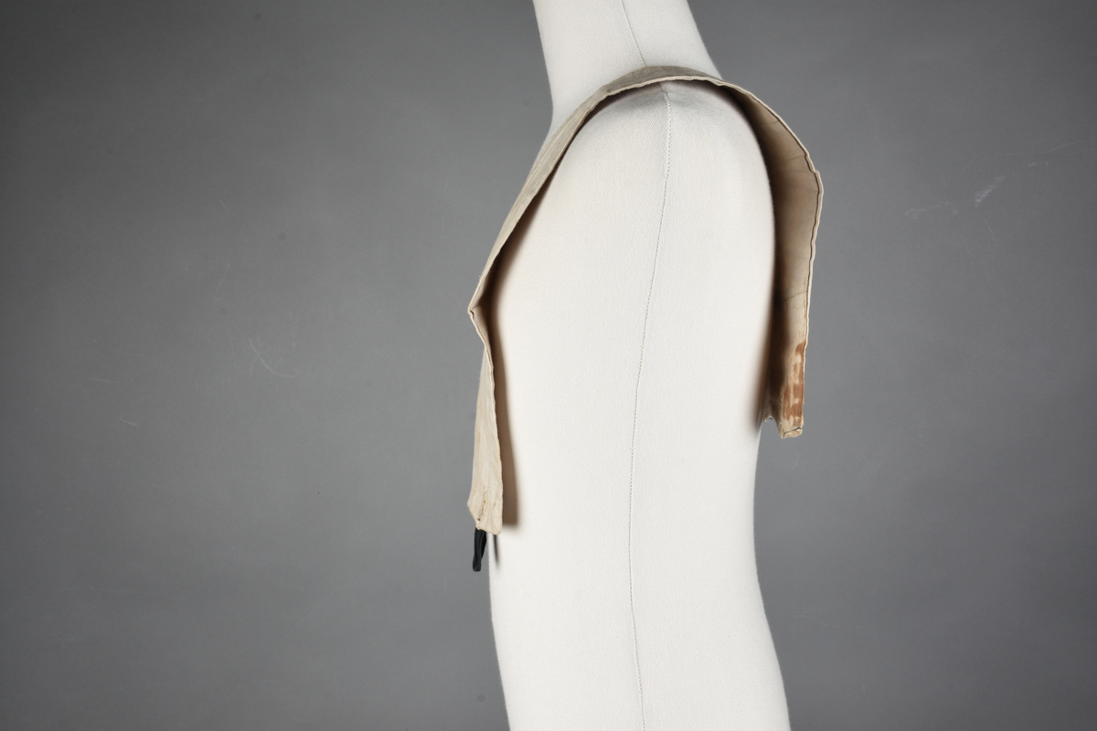 Matrosdress av ull og bomull. Bluse (A), benklær (B), livstykke (C) og matroskrave (D). Bluse med rett form og snøring i halsen. Legg på ermene. Lomme med rødt lommetørkle. Rød snor om skulder, Flagg- og våpenmerke. Benklær/bukse er åpen med knapp i begge sidene. Knelengde. Tre knappper på hvert bein, seks oventil. Grått livstykke til å feste buksen på. Knapphull og hemper. Matroskrave av mørkeblå silke med fire hvite striper langs den ytre kanten. To sorte bendel-knytebånd.