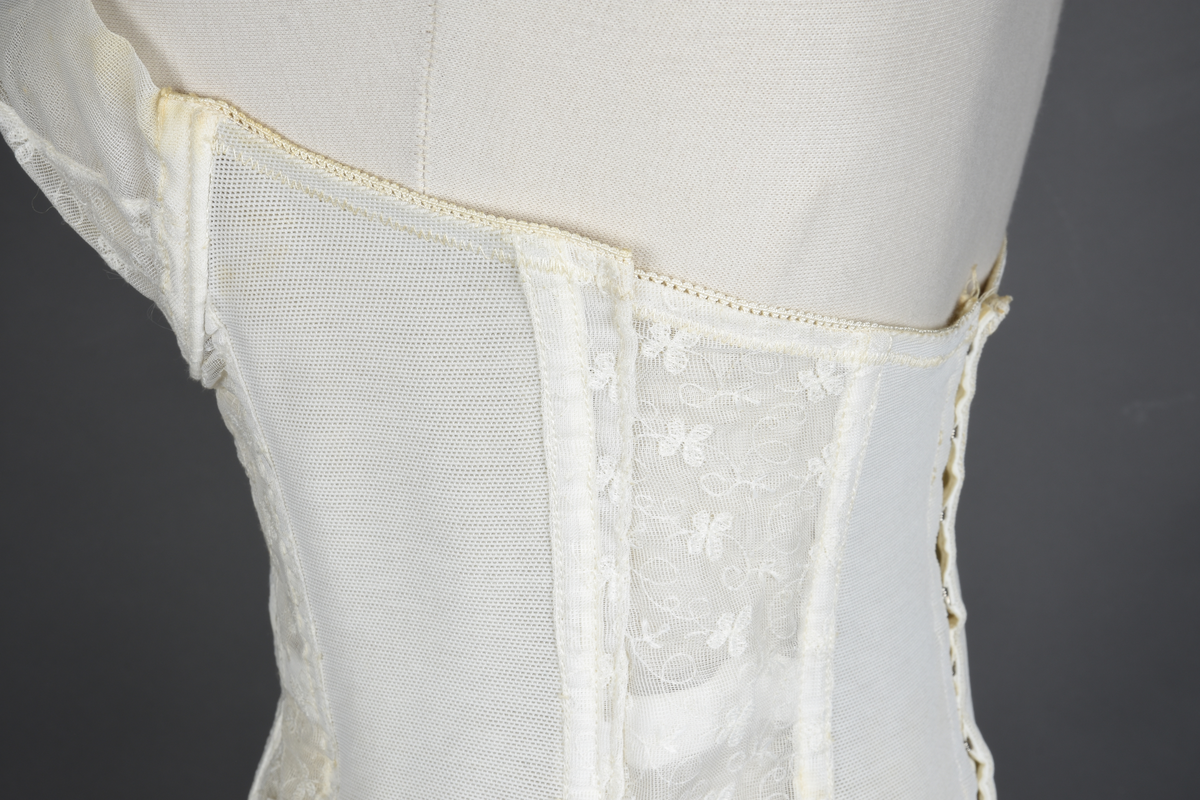 Brystholder av blondestrikk, med spiler. Både korsettspiler og cup-spiler. Lang form. Lukkes bak med hekter.