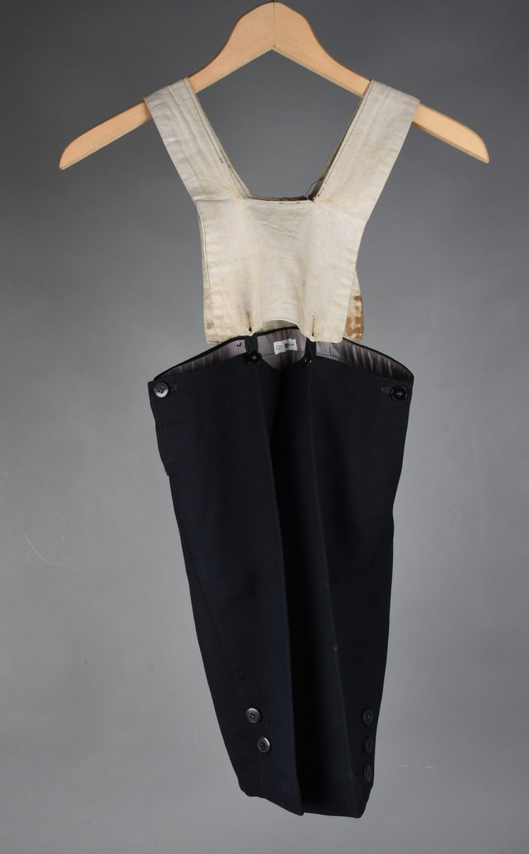 Matrosdress av ull og bomull. Bluse (A), benklær (B), livstykke (C) og matroskrave (D). Bluse med rett form og snøring i halsen. Legg på ermene. Lomme med rødt lommetørkle. Rød snor om skulder, Flagg- og våpenmerke. Benklær/bukse er åpen med knapp i begge sidene. Knelengde. Tre knappper på hvert bein, seks oventil. Grått livstykke til å feste buksen på. Knapphull og hemper. Matroskrave av mørkeblå silke med fire hvite striper langs den ytre kanten. To sorte bendel-knytebånd.