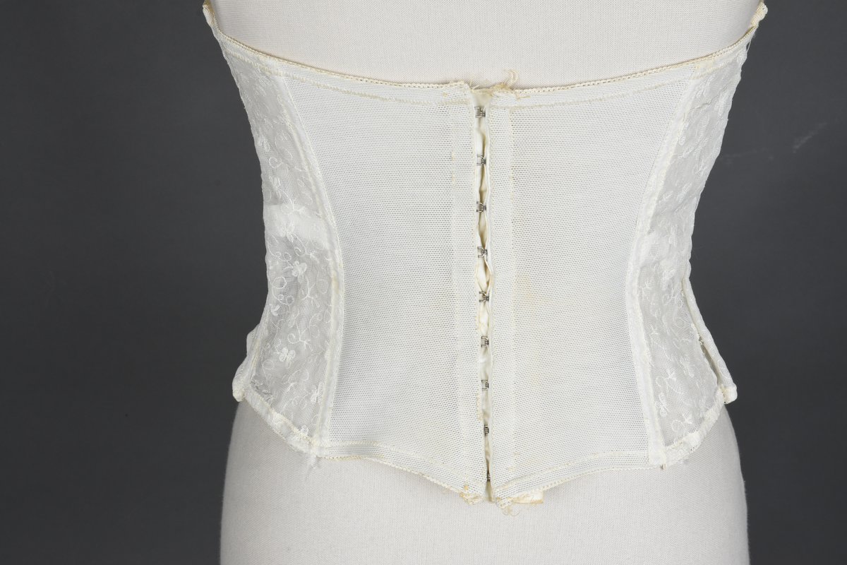 Brystholder av blondestrikk, med spiler. Både korsettspiler og cup-spiler. Lang form. Lukkes bak med hekter.