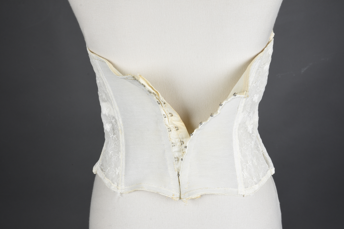 Brystholder av blondestrikk, med spiler. Både korsettspiler og cup-spiler. Lang form. Lukkes bak med hekter.