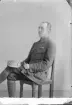 Porträtt av en man i militär uniform som sitter på en stol, med mössan i knät.