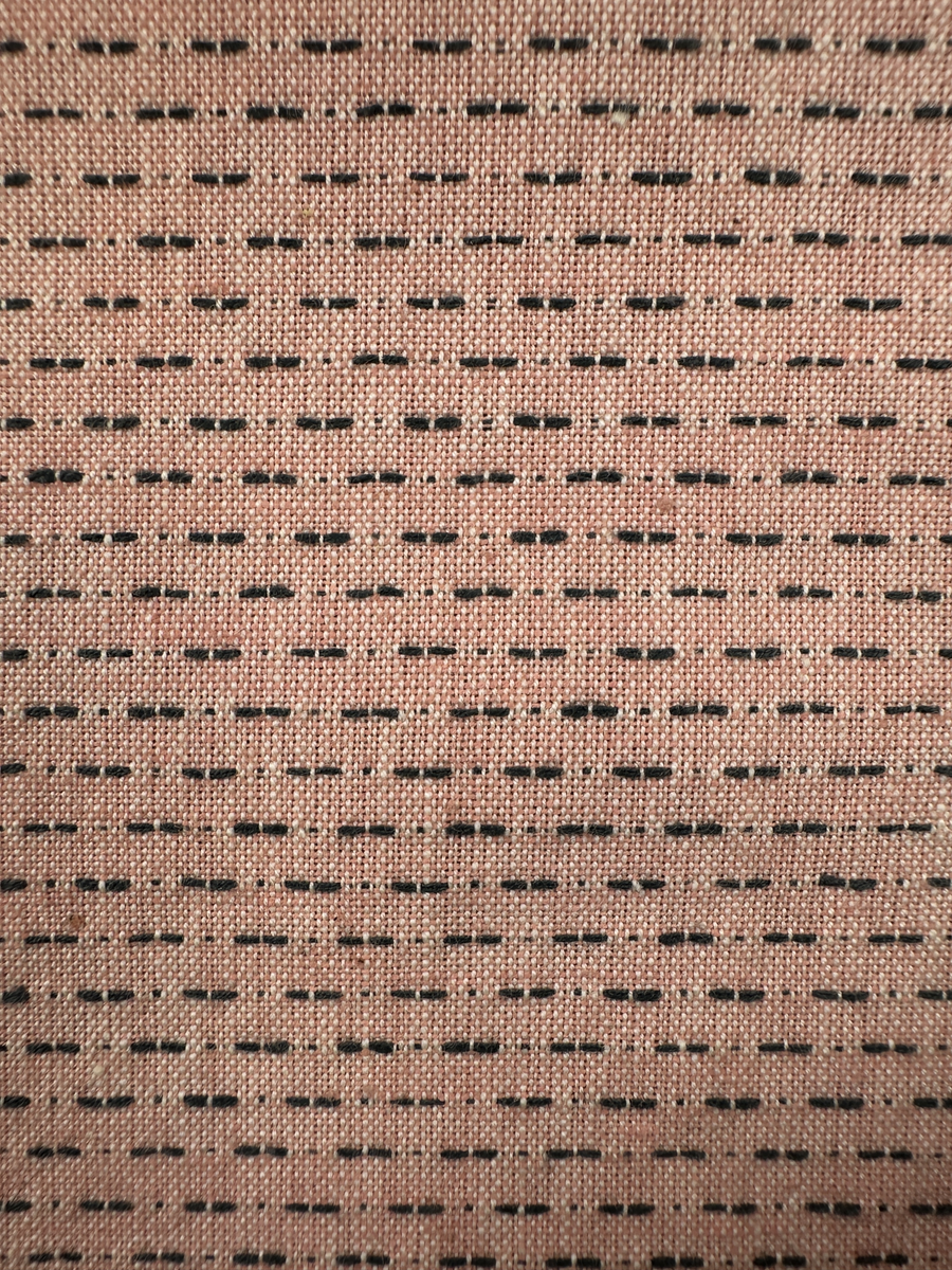 Rosa förkläde, handvävt i tuskaft med inslag av bruna "hopprosor" i bomullgarn. Förklädet har två utanpåhängande *fickor med smocksöm i övre kant. Förklädets midjelinje har också smocksöm sydd med svart tråd i 3mm glesa rader. Traskanten upptill är nervikt mot avigsidan och dolt av ett handvävt band i varprips av bomullsgarn. Bandet är fastsytt med smygstygn runt om samt fortsätter som knytband 62 och 64cm ut på var sida. Långsidorna och nederkant har 3mm respektive 17mm bred dubbelvikt fåll, som är fastsydd med smygstygn. 
* Fickdelen (ca 15x23,5cm) lagd räta mot räta på förklädet är fastsytt med en raksöm ca 8cm lång längs ena fickdelens kortsida. Kortsidans traskant, gömd i en 8mm bred dubbelvikt fåll, vikt mot fickans insida är sydd med smygstygn. Den andra kortsidan är fållad på samma sätt innan den sytts med smocksöm i 5mm glesa rader. Därefter är fickdelen vikt (botten) räta mot räta och ihopsydd med raksöm längs långsidorna, men fickans utsida med smocksöm är lagd 10mm ovanför för att dölja den andra kortsidans fåll. Denna del, 10mm, har sytts fast och fållats på insidan med smygstygn. Se bilder 5-11 på fickan.