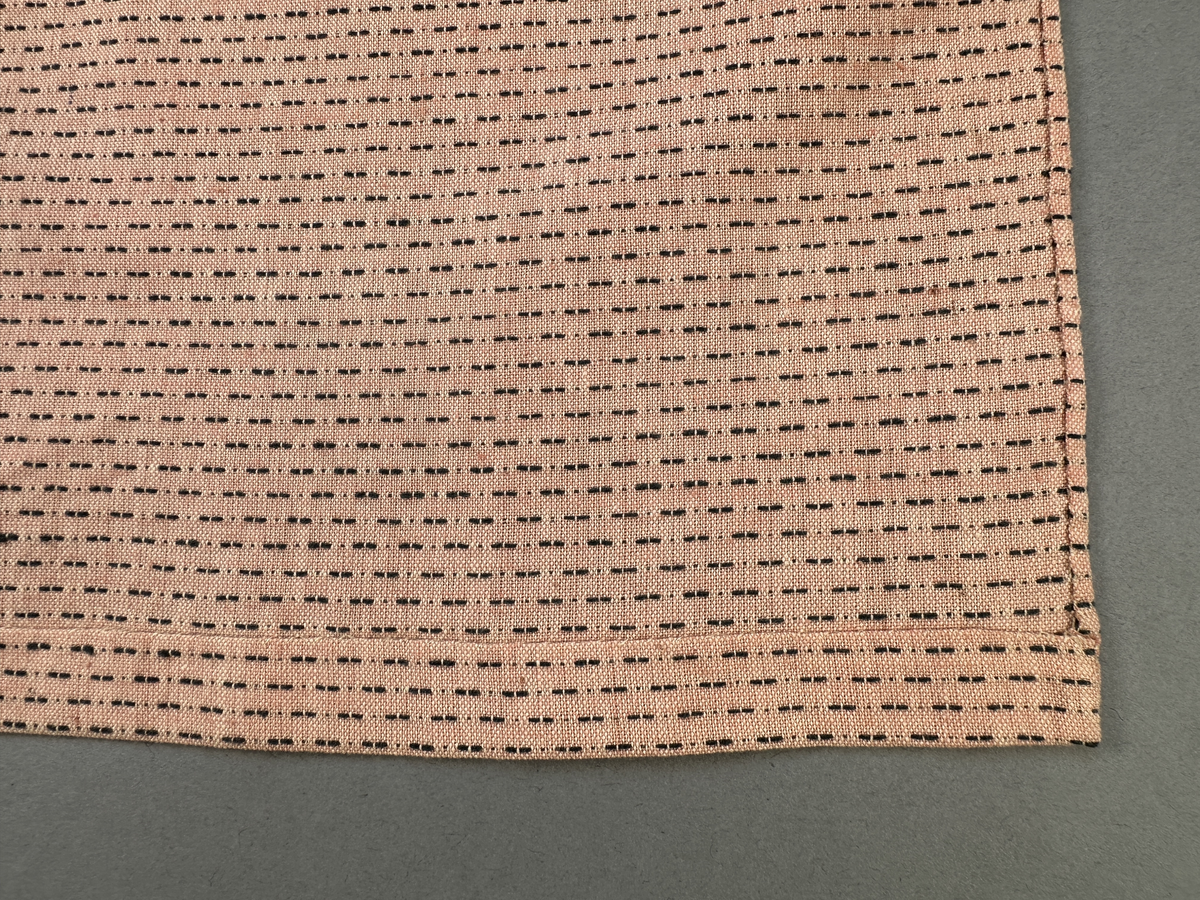 Rosa förkläde, handvävt i tuskaft med inslag av bruna "hopprosor" i bomullgarn. Förklädet har två utanpåhängande *fickor med smocksöm i övre kant. Förklädets midjelinje har också smocksöm sydd med svart tråd i 3mm glesa rader. Traskanten upptill är nervikt mot avigsidan och dolt av ett handvävt band i varprips av bomullsgarn. Bandet är fastsytt med smygstygn runt om samt fortsätter som knytband 62 och 64cm ut på var sida. Långsidorna och nederkant har 3mm respektive 17mm bred dubbelvikt fåll, som är fastsydd med smygstygn. 
* Fickdelen (ca 15x23,5cm) lagd räta mot räta på förklädet är fastsytt med en raksöm ca 8cm lång längs ena fickdelens kortsida. Kortsidans traskant, gömd i en 8mm bred dubbelvikt fåll, vikt mot fickans insida är sydd med smygstygn. Den andra kortsidan är fållad på samma sätt innan den sytts med smocksöm i 5mm glesa rader. Därefter är fickdelen vikt (botten) räta mot räta och ihopsydd med raksöm längs långsidorna, men fickans utsida med smocksöm är lagd 10mm ovanför för att dölja den andra kortsidans fåll. Denna del, 10mm, har sytts fast och fållats på insidan med smygstygn. Se bilder 5-11 på fickan.