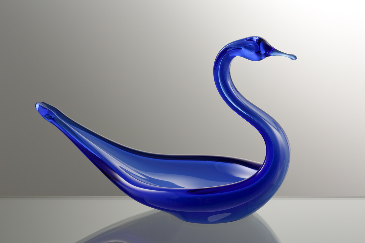 Prydnadsglas i form av en svan.
Kroppens kärna är ett opakt underfång i vitt, som försetts med ett yttre klarglasskikt i blått.

Inskrivet i huvudkatalogen tidigast 1988.