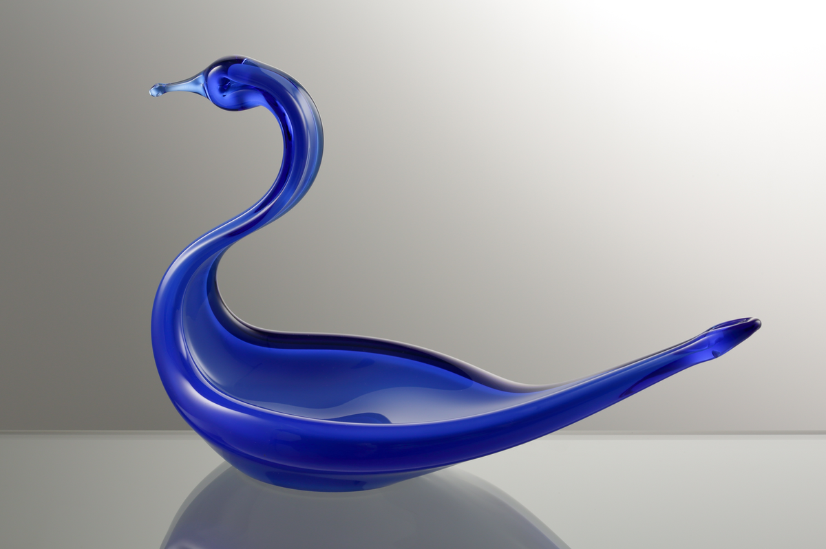 Prydnadsglas i form av en svan.
Kroppens kärna är ett opakt underfång i vitt, som försetts med ett yttre klarglasskikt i blått.

Inskrivet i huvudkatalogen tidigast 1988.