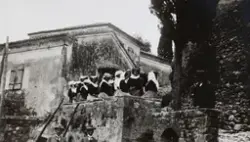 Kvinner ikledd søndagsdrakt i en landsby nær slottet Achilleion på Korfu. To menn skimtes i forgrunnen. Fotografert april 1925 under ekteparet Egebergs cruise i Middelhavet.