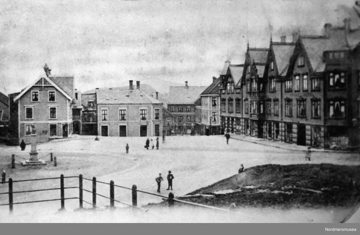 Repro av et postkort utgitt av Kristian Kvandes Papirhandel i Kristiansund. Her ser ver fra torvet på Kirklandet i Kristiansund, med Grand hotell til høyre. Ellers så ser vi Christiestøtten til venstre