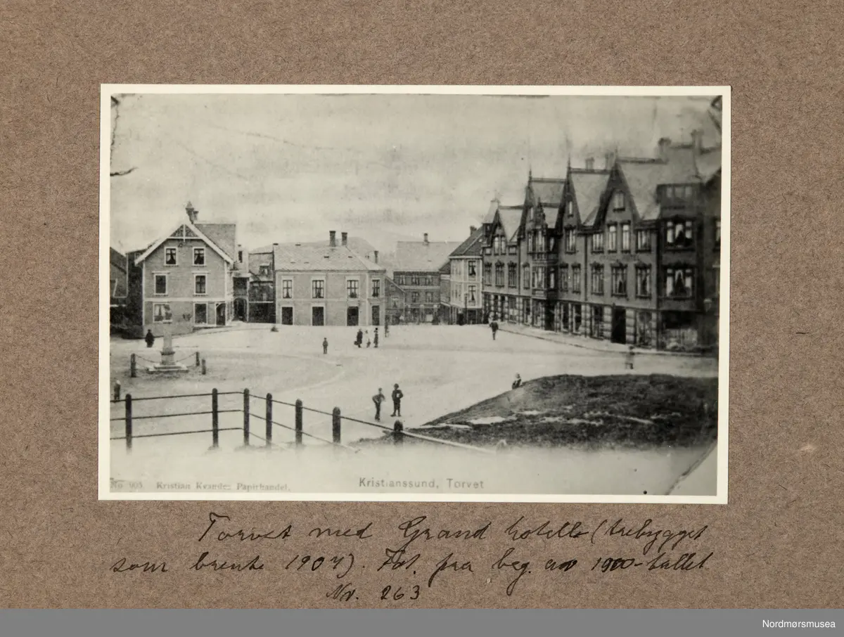 Repro av et postkort utgitt av Kristian Kvandes Papirhandel i Kristiansund. Her ser ver fra torvet på Kirklandet i Kristiansund, med Grand hotell til høyre. Ellers så ser vi Christiestøtten til venstre
