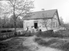 Familj uppställd framför ett hus. Okänd plats, 1905.