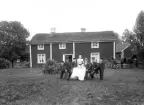 Familj vid trädgårdsbord, framför okänt bostadshus. Ca. 1900.