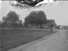 Lanthandel i Åkerby, Ljuder, vid en landsväg. Ca 1900. Några personer står vid huset och vägen.