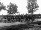 En samling herrar med cyklar, uppställda utmed en grusväg. Ca 1912.