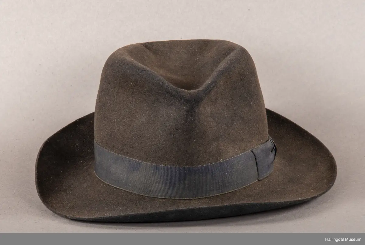 a) åpen mannstrøye, b) mannsvest, c) langbukse, d) halsklut og tilhørende også e) hatt. Open trøye m svarte knappar, dobbelspent vest. Svart m blått, kvitrundut for, rindutt vestebakklut. Sauma maskinsaum til dekor på ermekragar og framside. Ferdig sydd halsklut i silketøy. Filthatt med silkebånd og silkefor.