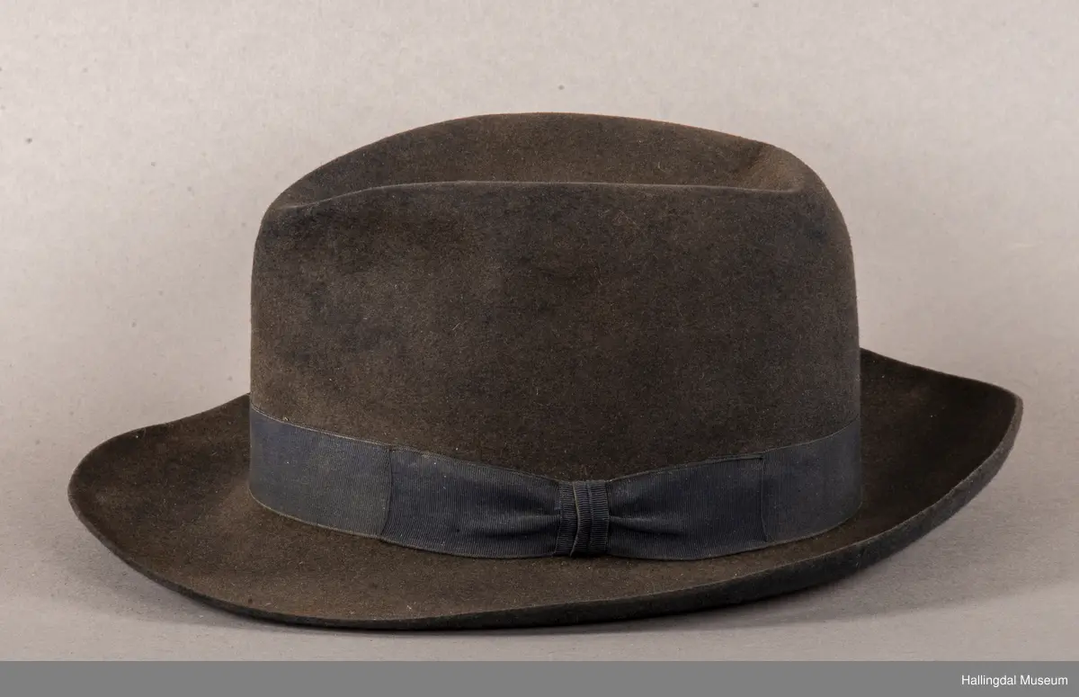 a) åpen mannstrøye, b) mannsvest, c) langbukse, d) halsklut og tilhørende også e) hatt. Open trøye m svarte knappar, dobbelspent vest. Svart m blått, kvitrundut for, rindutt vestebakklut. Sauma maskinsaum til dekor på ermekragar og framside. Ferdig sydd halsklut i silketøy. Filthatt med silkebånd og silkefor.