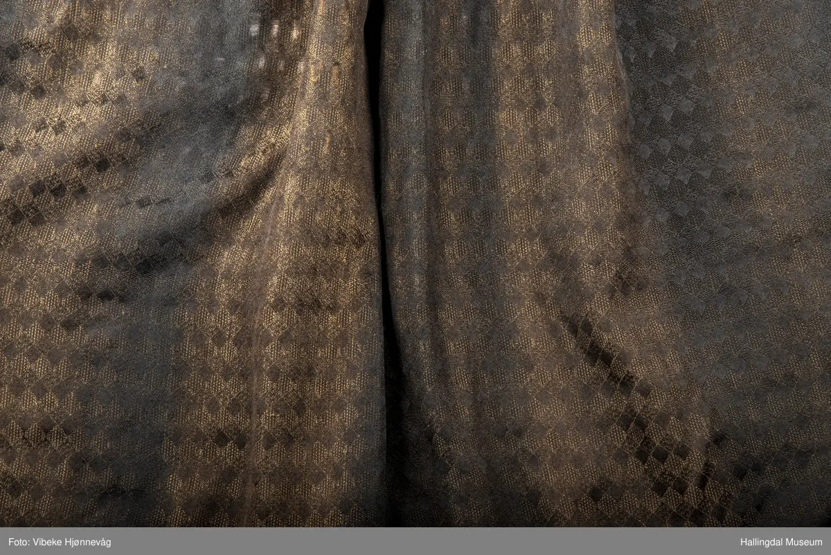 Svart Ulldamask, kroklisser, flanillgådn, eplebånd (fløyel), fløyelsbånd og svart bomullstoff. Lilla og svart bånd, røde kroklisser. Plattsømbroderi: rødt, mørk rødt, rosa, lys rosa, blått, hvitt og lys grønt.
Lengde: 104 cm, bredde: 90 cm, bredde oppe: 41 cm, bredde bånd oppe: 4 cm, bredde plattsømsbroderi nederst: 8,5 cm.