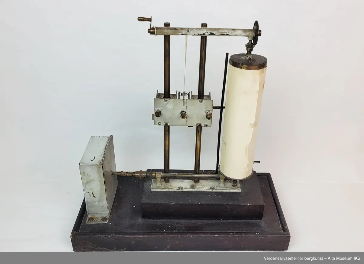 Instrument for måling av vindstyrke og vindretning. Metallstativ med skriveanretning som skriver på fastmontert papirrull. Drivermekanisme ved siden av, alt montert på en treplate.