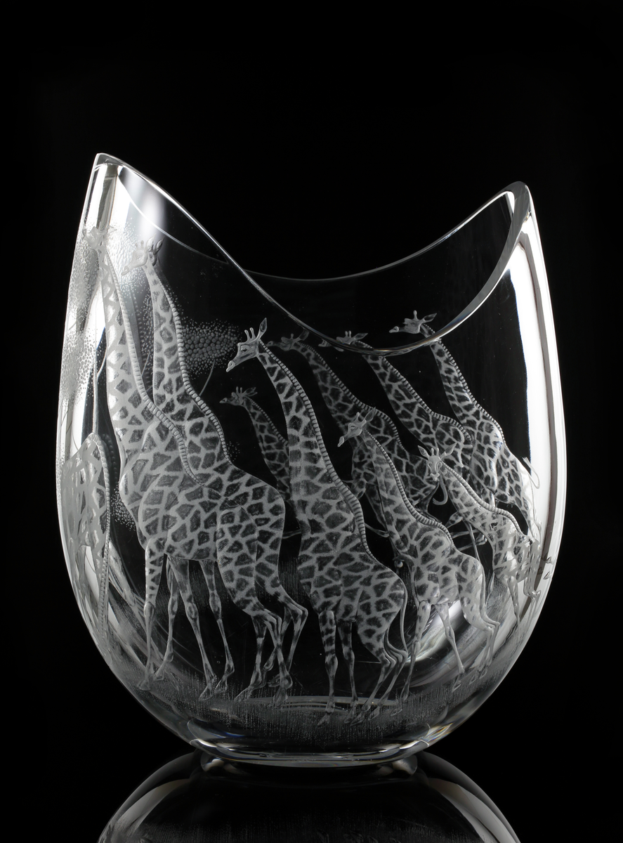 Vas. "Safari". LG 248, 22. Designer: Vicke Lindstrand.
Tillplattat slutet äggformat (oval), med vågigt nedbuktande överkant som är sågad.
Giraffer och träd i omvänd relief.
Ofärgat klarglas.
Väggtjocklek: 8 mm. 

Inskrivet i huvudkatalogen 1966. 

Kataloger:
Katalog nr. 2, 1959-1960. 

Vicke Lindstrand (1904-1983) konstnär, glasdesigner m.m. Verksam på Kosta 1950-1973.