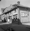 Dåvarande Ågatan 43 i Linköping, Ekmanska gården kallad. Bakom namnet står plåtslagaren August Leonard Ekman som från 1892 drev sitt plåtslageri från gården. I gatuhuset drev han en bosättningsaffär vars inriktning ännu bestod vid fototillfället 1958. Rörelsens, och hela husets, öde på platsen var dock beseglat vid tiden. Byggnaden räddades lyckligtvis för ny placering i friluftsmuseet Gamla Linköping.